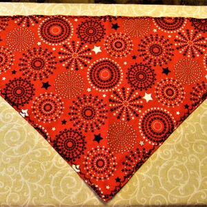 May include: Red bandana with a white and black firework pattern. The bandana is folded into a triangle shape.