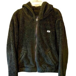 May include: Dark green hooded zip-up jacket with a fuzzy, textured exterior. The jacket features a full-length zipper, a hood, and a small white patch with "A&F" on the chest. The jacket has two front pockets and a soft, plush appearance.