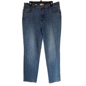 May include: Light blue denim jeans with a classic five-pocket design. The jeans have a straight leg cut and a button and zipper closure. The jeans are hanging on a black hanger.