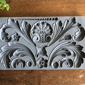 May include: A gray silicone mold with the text "IOD" in the top left corner. The mold features a variety of intricate floral and scroll designs.