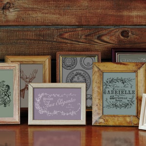 May include: A collection of vintage-style picture frames with various designs and text. The frames are in different sizes and colors, including wood, white, and purple. The images inside feature botanical illustrations, a coat of arms, and French text.