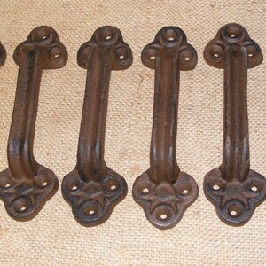 May include: Six antique-style cast iron door pulls with a decorative floral design. The pulls are dark brown and have a rustic finish.