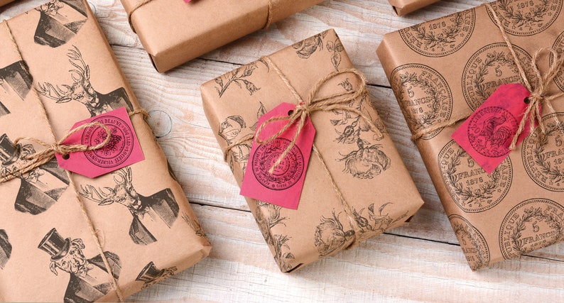 May include: Several wrapped gifts with brown paper and twine. The paper is printed with various designs, including deer, floral patterns, and coin illustrations. Each gift has a pink tag tied with twine.