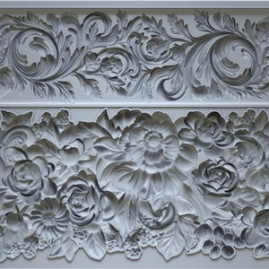 May include: A gray, rectangular mold featuring two ornate floral designs. The top design showcases scrolling leaves and flowers, while the bottom design features roses and other blooms. The mold is labeled "TRIMMINGS 4 IOD".