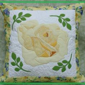 Peut inclure: Un coussin brodé avec une rose blanche et jaune et des feuilles vertes sur un fond blanc. Le coussin a une bordure à motifs floraux jaunes et bleus.