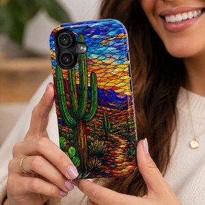 May include: A colorful phone case featuring a desert landscape with a large green cactus, smaller cacti, and a path. The background showcases a sunset with blue, orange, and yellow hues. The case has a glossy finish.