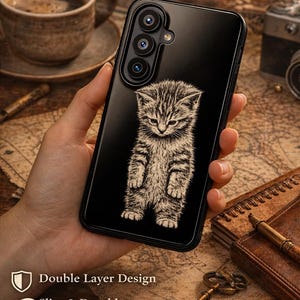 May include: Black phone case with a detailed illustration of a standing kitten. The case features the text "Shockproof Protect Your Phone", "Double Layer Design", and "Slim & Durable". Designed for iPhone 17 & Samsung 2026 models.