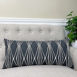 May include: A long, rectangular throw pillow with a black and white geometric pattern. The pillow is made of a soft, textured fabric and has a subtle sheen.