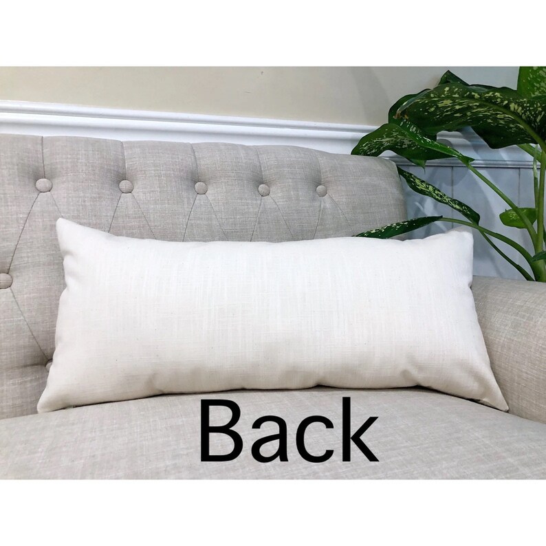 May include: A plain white rectangular cushion with a subtle texture, placed on a light grey tufted sofa. The word "Back" is printed in black below the cushion.