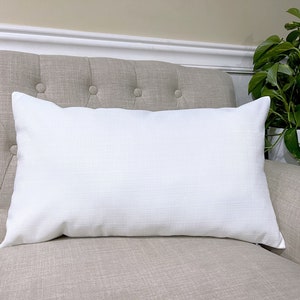 May include: A white rectangular pillow with a textured surface, sitting on a light brown couch.