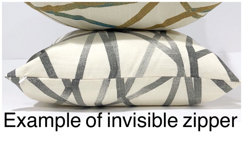 May include: Two decorative throw pillows. The bottom pillow has a cream-colored background with a gray geometric pattern. The top pillow has a cream-colored background with a gold and teal pattern. The text "Example of invisible zipper" is at the bottom.