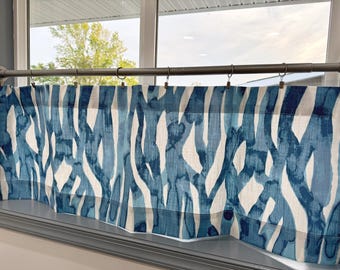 May include: Blue and white patterned window valance. The fabric features a watercolor-like design of vertical, abstract shapes in varying shades of blue against a white background. The valance is hung on a metal rod with clips.