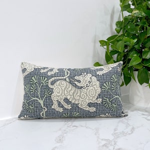 May include: A rectangular throw pillow with a blue background and a white stylized lion design. The lion is surrounded by green leafy branches.