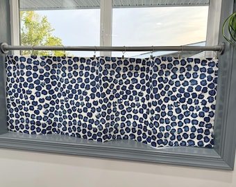 May include: A blue and white patterned valance curtain hangs in a window. The fabric features a repeating pattern of navy blue spots on a white background. The curtain is mounted on a silver rod with metal rings.