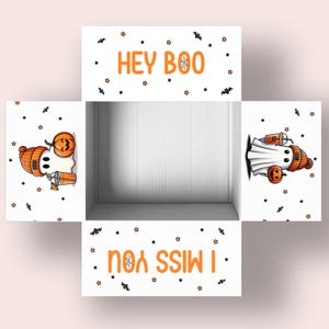 May include: A white Halloween-themed gift box with orange text that reads "HEY BOO" and "I MISS YOU". The box features illustrations of ghosts wearing orange beanies and holding pumpkin-shaped lanterns and drinks. Black bats and stars decorate the box.