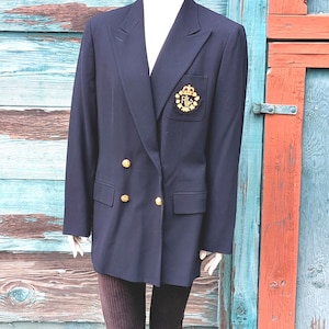 May include: Navy blue blazer with gold-colored buttons and a crest emblem on the pocket. The double-breasted jacket has a classic design and is displayed on a mannequin. The blazer is a timeless piece of apparel.