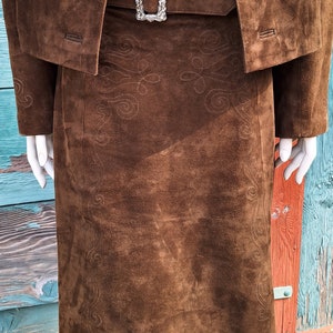 A close up view of a brown suede skirt with embroidered details. The skirt has a brown leather belt with a silver buckle.