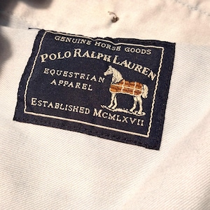 A tag from a pair of denim riding jods by Ralph Lauren. This is the inside label showing a horse with a blanket on and Polo Ralph Lauren written across the top and Equestrian Apparel under that. Established  1967 is on the bottom, the tag is dark navy