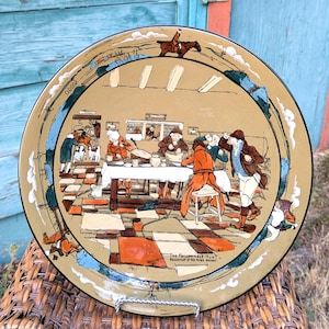 May include: A decorative plate with a detailed illustration depicting a hunting scene. The plate features a central image of people gathered around a table, with a border of blue and white accents. The text "The Fallowfield Hunt Breakfast at the Peers Arms" is visible.