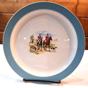 May include: A vintage ceramic bowl with a blue rim and a hunting scene illustration. The scene features two riders on horseback, a fox hunt, and a blue sky background.