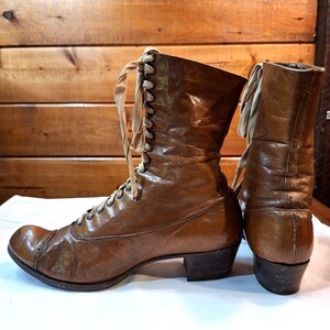 left side detail of a pair of leather ladies Victorian boots with tan laces and low heels. The boots are brown leather with rounded toes.