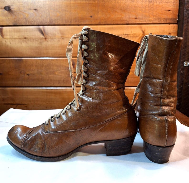 left side detail of a pair of leather ladies Victorian boots with tan laces and low heels. The boots are brown leather with rounded toes.