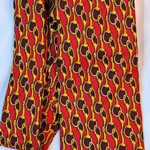 May include: A red silk tie with a repeating pattern of gold horse bit chains.