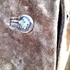 A close-up of a brown suede jacket with a silver and horn button featuring a leaf design.