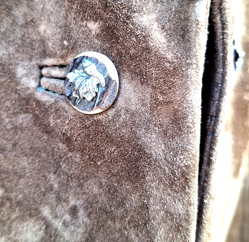 A close-up of a brown suede jacket with a silver and horn button featuring a leaf design.