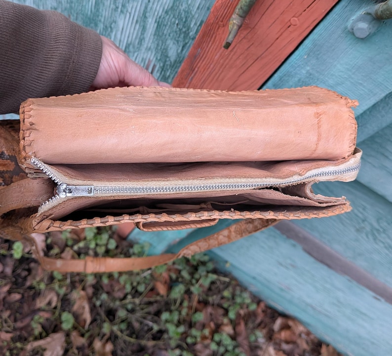 Top down view of the inside of a structured snakeskin purse. The inside lining is light beige leather with a zippered center and pouches on either side