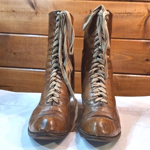 Front view of a pair of brown leather ladies Victorian boots with low heels and tan laces. The boots are narrow and long with above the ankle height