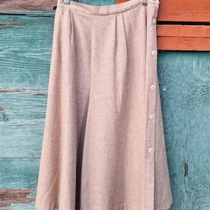 May include: A brown wool skirt with a side button closure. The skirt is hanging on a hanger against a wooden background.