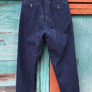 A pair of dark blue denim riding pants with reinforced stitching on the knees and seat. The pants have a classic five-pocket design and a straight leg fit.