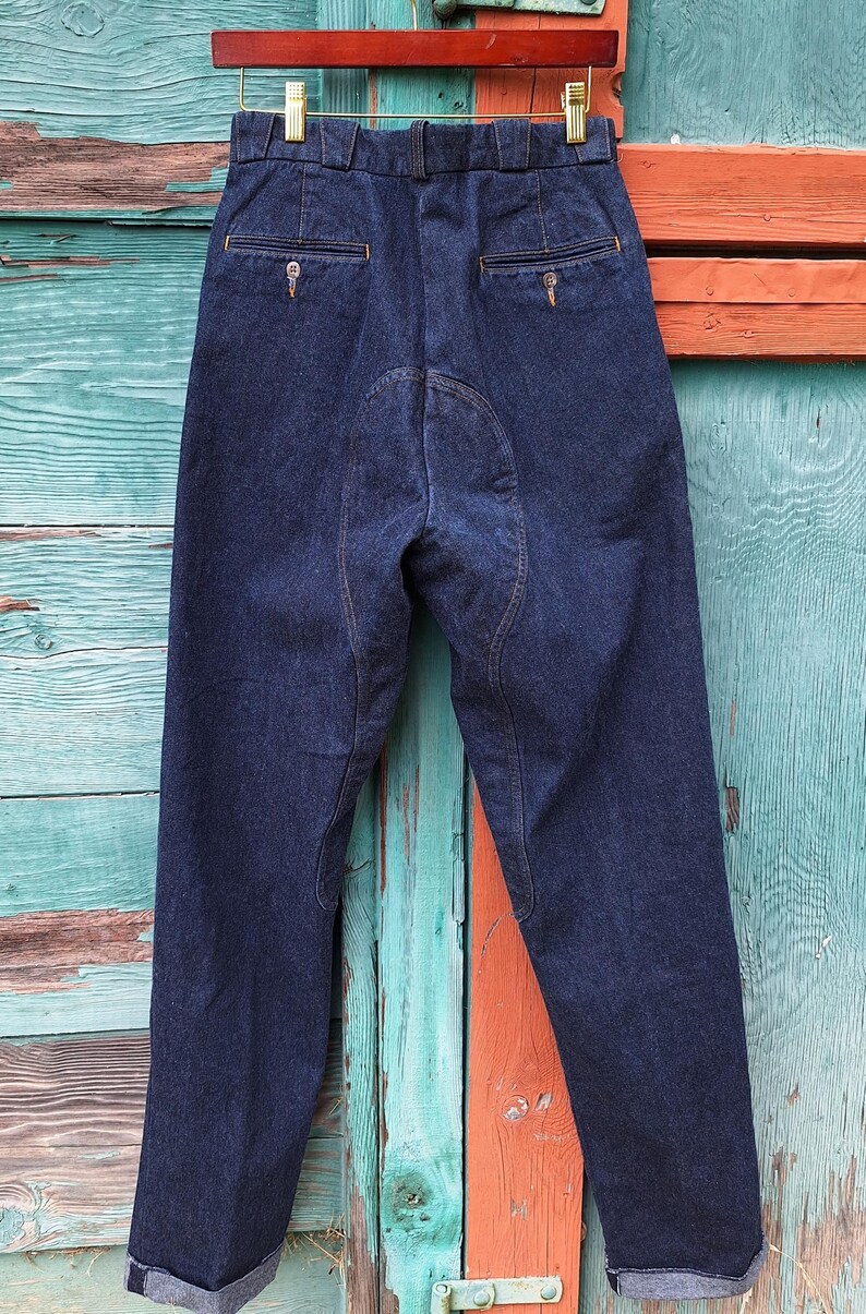 A pair of dark blue denim riding pants with reinforced stitching on the knees and seat. The pants have a classic five-pocket design and a straight leg fit.