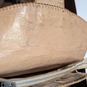 The inside flap of a structured snakeskin handbag. The leather is light beige with exposed stitching detail. The inside of the purse has a zippered center