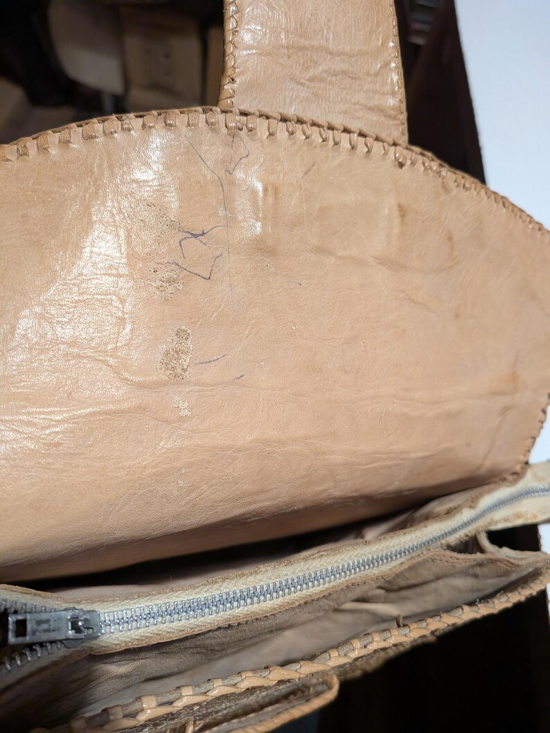 The inside flap of a structured snakeskin handbag. The leather is light beige with exposed stitching detail. The inside of the purse has a zippered center