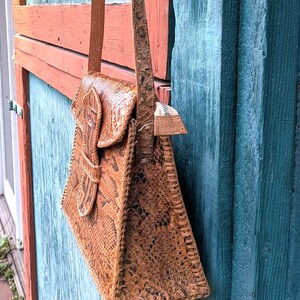 Sid view of a structured snakeskin leather purse that is chestnut and black. The purse has a long strap and a tab front closure