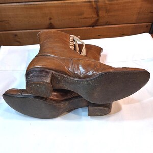 Bottom view of the soles of a pair of ladies brown leather Victorian boots with tan laced fronts. The soles have dark leather with tan stitching .