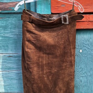 A brown suede skirt with a decorative embroidered design. The skirt has a belt with a silver buckle and a zipper closure.
