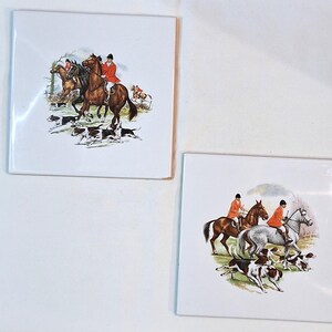 May include: Two vintage ceramic tiles depicting a hunting scene with riders on horseback and hounds chasing a fox. The tiles are white with a colourful illustration.