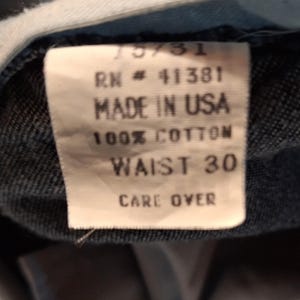 A white tag with black text that reads '75/31', 'RN # 41381', 'Made in USA', '100% Cotton', 'Waist 30', and 'Care Over'.