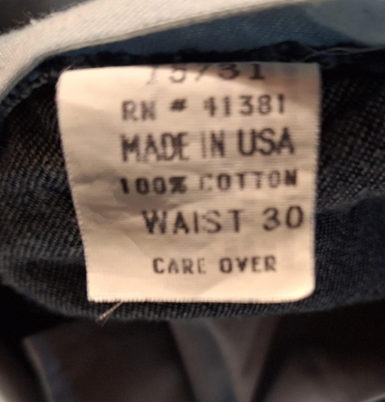A white tag with black text that reads '75/31', 'RN # 41381', 'Made in USA', '100% Cotton', 'Waist 30', and 'Care Over'.