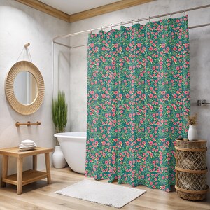 May include: Teal shower curtain with a repeating floral pattern of pink flowers and green leaves. The bathroom features a wooden side table, a round mirror, and a white bathtub.