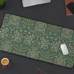 Peut inclure: Tapis de bureau rectangulaire avec un motif floral détaillé dans les tons de vert, orange et jaune. Le tapis a une bordure noire et est conçu pour une souris et un clavier d'ordinateur. Une souris blanche est visible sur le tapis.