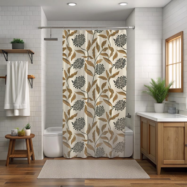 May include: A beige shower curtain with a repeating pattern of brown leaves and black, dotted floral clusters. The curtain hangs in a bathroom with white tile walls, a wooden vanity, and a small wooden stool.