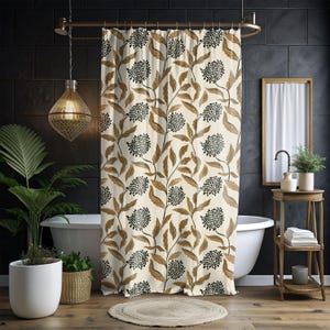 May include: Cream-colored shower curtain with a repeating pattern of brown leaves and black dotted flower clusters. The curtain hangs in front of a white bathtub, with a gold shower rod. The bathroom has dark tile walls and a wooden floor.