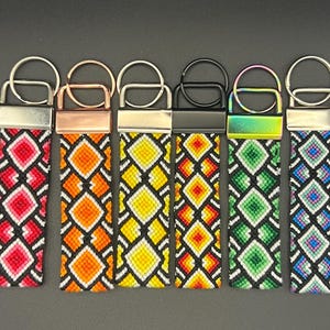 May include: Six colorful keychains with geometric diamond patterns. Each keychain features a different color scheme: red, orange, yellow, green, and blue. The keychains have metal hardware and a woven design.