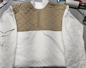 May include: A white and tan quilted jacket with a stand-up collar and a quarter-zip closure. The jacket features a quilted tan panel across the chest and upper back, with white sleeves and body. It has a pocket on the left sleeve.