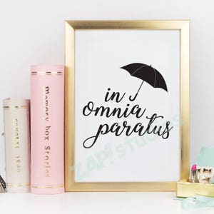 May include: A gold framed print with a black umbrella and the text "in omnia paratus" in a black script font.