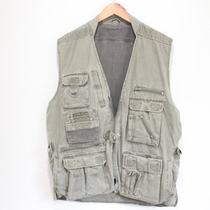 May include: Olive green utility vest with multiple pockets and a mesh back panel. The vest is hanging on a wooden hanger against a white background. Features multiple zippered and flap pockets.
